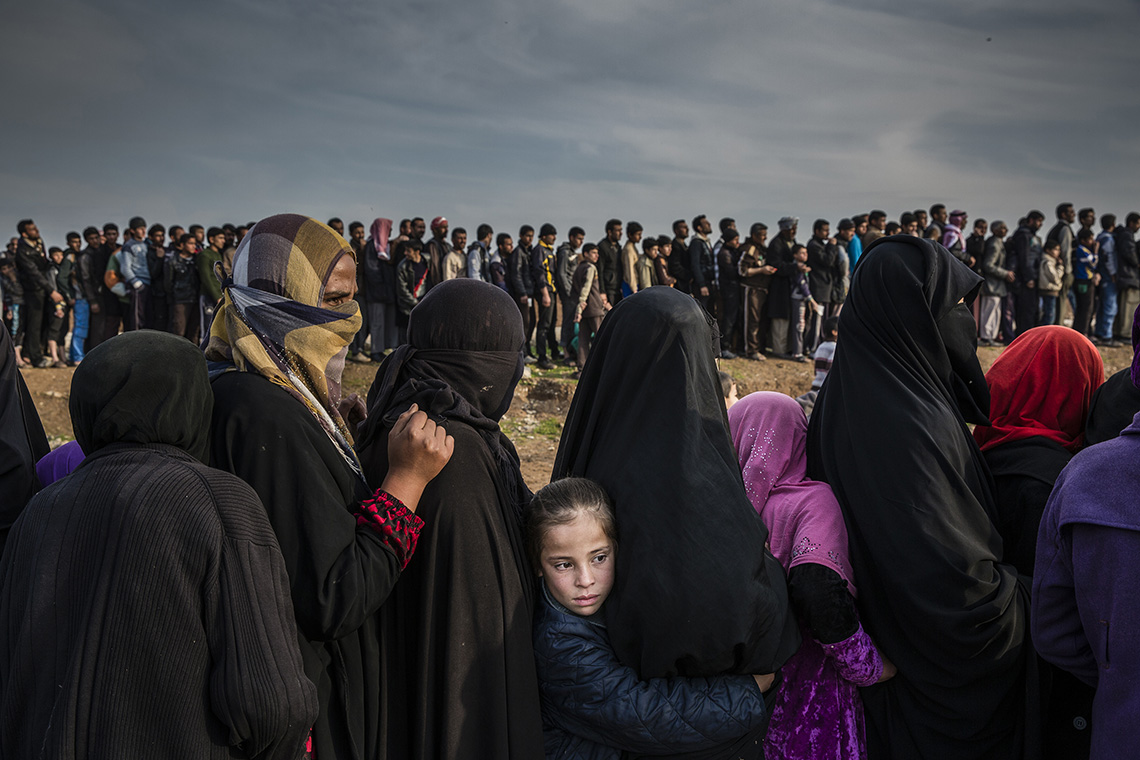 Civilians who had remained in west Mosul after the battle to take the city line up for aid in the Mamun neighbourhood. One girl turns her face to the masses while the others look on. Shot by Ivor Prickett.